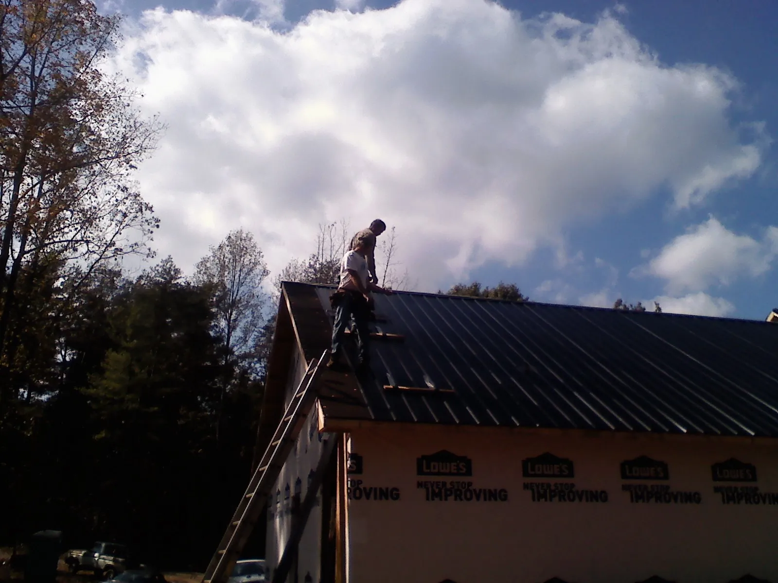Roofer fastening dark metal panels high against a cloudy sky, from a Roof Inspection job in Clarence