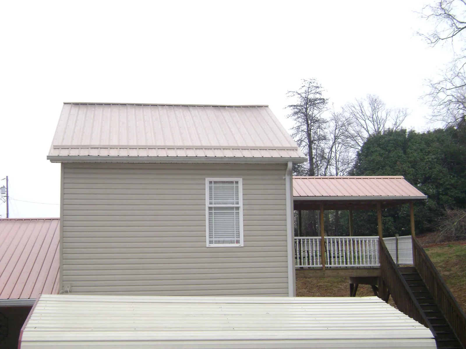 Tan metal roofs on a two story addition and attached porch, from a Roof Replacement job in Clarence
